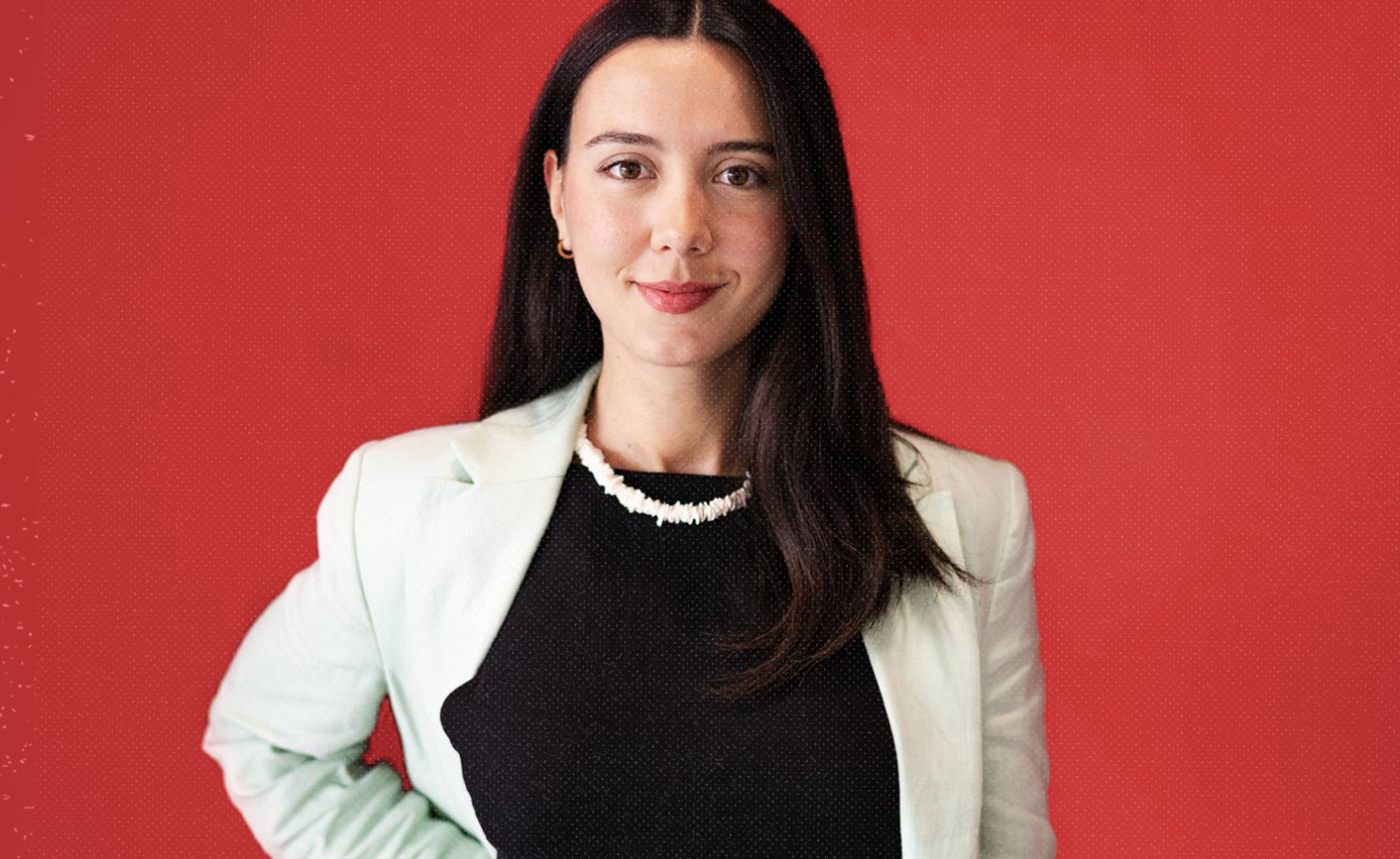 Foto de biografia da Leonor Caldeira. A Leonor aparece a meio corpo, a olhar directamente para a camera, com um sorriso confiante e um blazer branco, contrea um fundo vermelho.